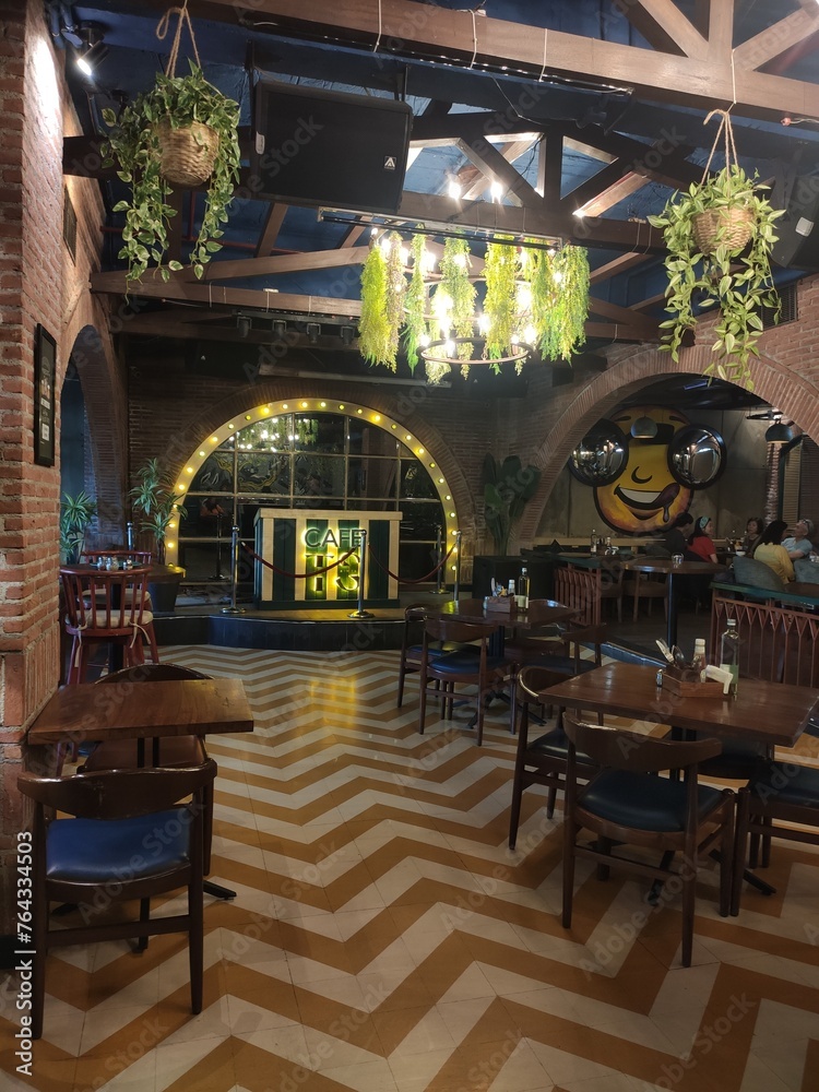 Intérieur d'un grand restaurant-bar indien avec simple décoration jardinière ou naturelle, des lierres ou de la fausse végétation sur les murs, plafond et lampadaires, ambiance chaleureuse 