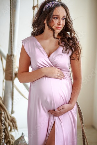 Portrait of beautiful pregnant woman with long curly hair in pink dress