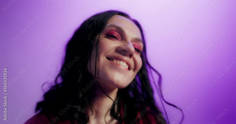 A woman with pink arrows on her eyes, dressed in casual clothes, smiles and dances standing on a pink background in the studio