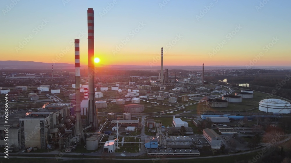 Tall chimneys of oil refinery with depot and huge storage tanks at sunset. Aerial