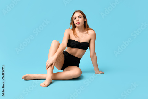 Attractive young woman in black underwear sitting against blue background © Pixel-Shot