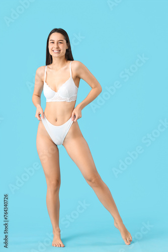 Slim young woman in white underwear on blue background