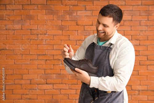 Male shoemaker repairing boot on brick background