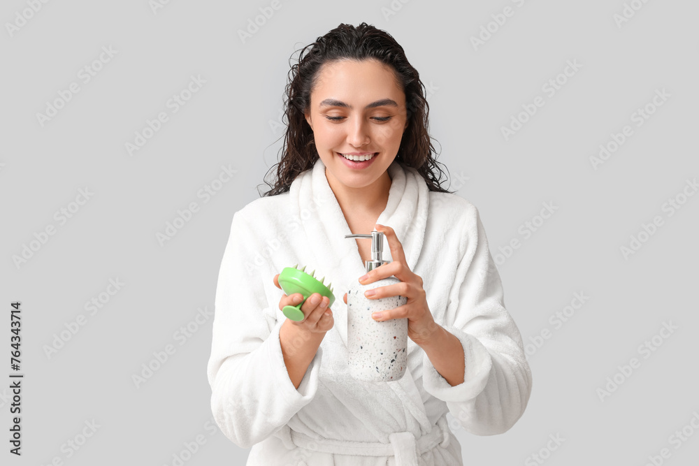 Beautiful young woman with hair scalp massager and shampoo on grey background Beautiful young woman with hair scalp massager and shampoo on grey background