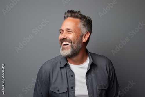 Handsome middle aged man laughing and looking away while standing against grey background