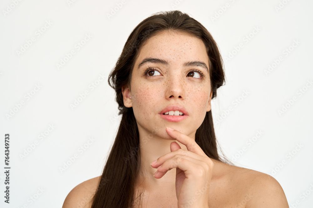 Young adult Latin woman, brunette girl with freckles on face looking away isolated on white background thinking choosing skin care cosmetic product for skin care ads. Beauty aesthetic portrait. Young adult Latin woman, brunette girl with freckles on face looking away isolated on white background thinking choosing skin care cosmetic product for skin care ads. Beauty aesthetic portrait.