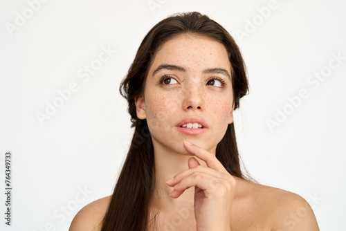 Young adult Latin woman, brunette girl with freckles on face looking away isolated on white background thinking choosing skin care cosmetic product for skin care ads. Beauty aesthetic portrait.