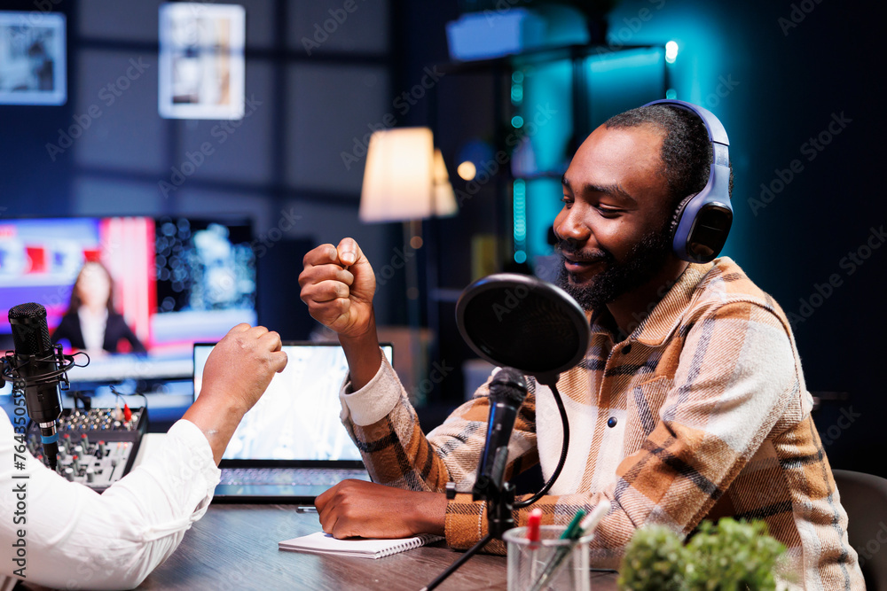 Smiling black man doing fist bump with african american presenter before starting live radio broadcast. Cheerful male influencer greeting guest during a recording session of online talk show.