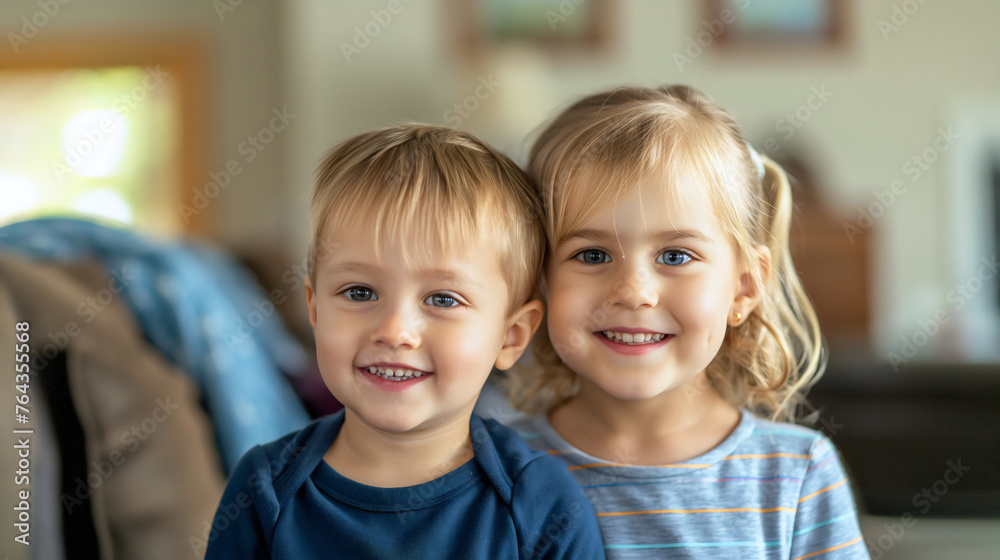 Young toddler preschool brother and sister sitting hugged on the sofa in the living room of home interior, smiling at camera. Little boy and girl, children family love, two siblings bonding hugged