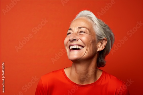 Portrait of happy senior woman laughing and looking up on orange background