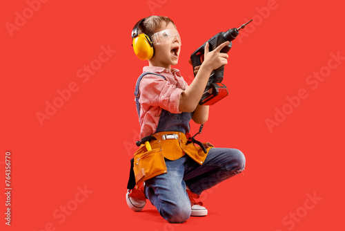 Cute little builder with drill on red background photo