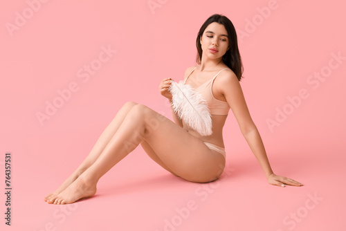 Pretty young woman with soft feather sitting against pink background. Epilation concept