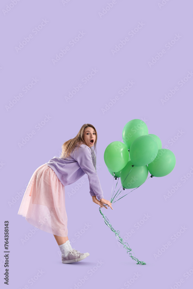 Shocked young woman with green balloons on lilac background