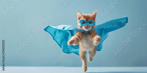 An adorable orange tabby cat dressed as a superhero with a blue cape, appearing to fly against a soft blue background.