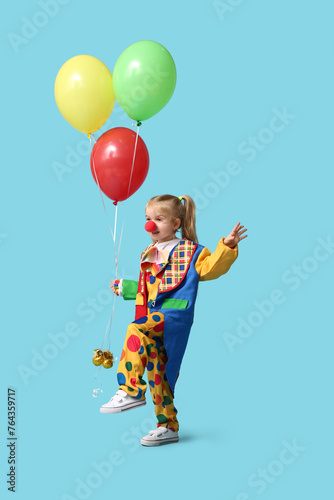 Cute little girl in clown costume with balloons on blue background