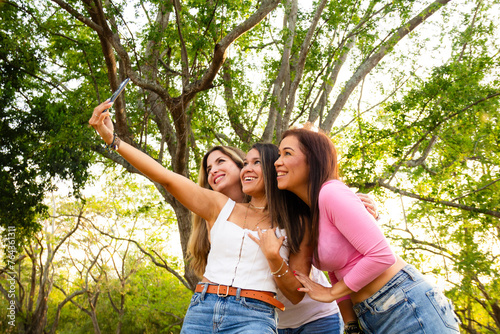 three casual hispanic female friends taking a self portrait or selfie in a park