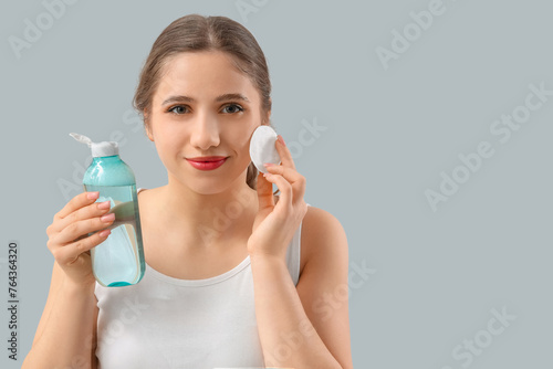 Young woman with micellar water and cotton pad on light background, closeup