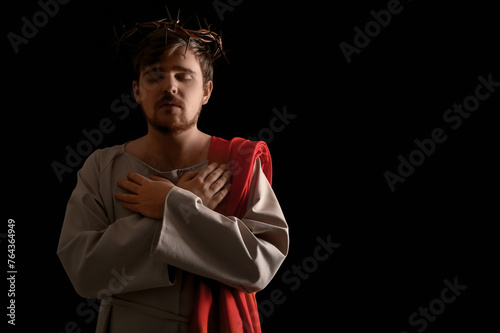 Man in Jesus robe and crown of thorns crossing hands with light on black background