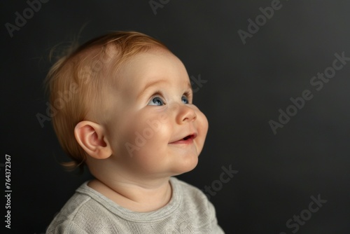 A baby with blonde hair and blue eyes is smiling and looking up at the camera