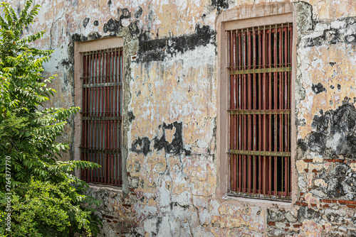 Cartagena, Colombia - July 25, 2023:Couple of grilled windows in ancient wall on Baluarte de San Ignacio rampart and bastion. Some green foliage photo