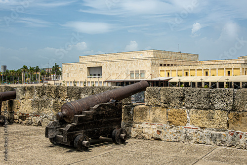 Cartagena, Colombia - July 25, 2023: Cannon on Baluarte de San Ignacio rampart and bastion under. blue cloudscape. Beige stone Convention Center building in back photo