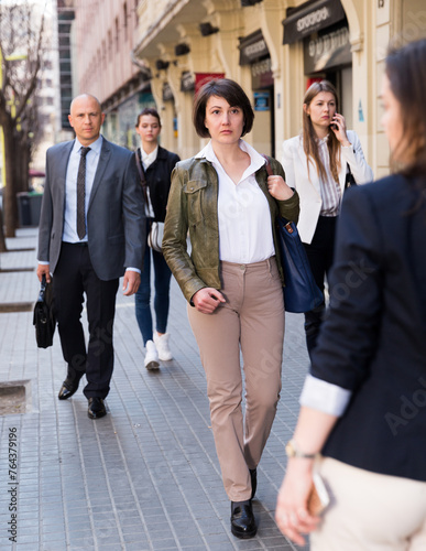 Full-length portrait of adult woman in casual dress walking on city street in crowd of people