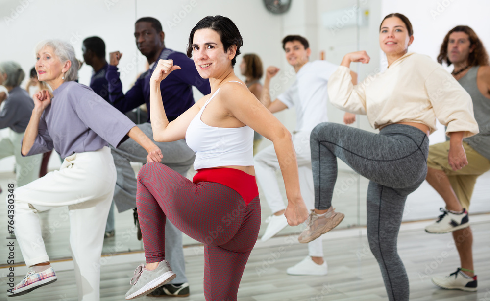 Fototapeta premium Happy young woman practising modern dance moves with other people in dance studio