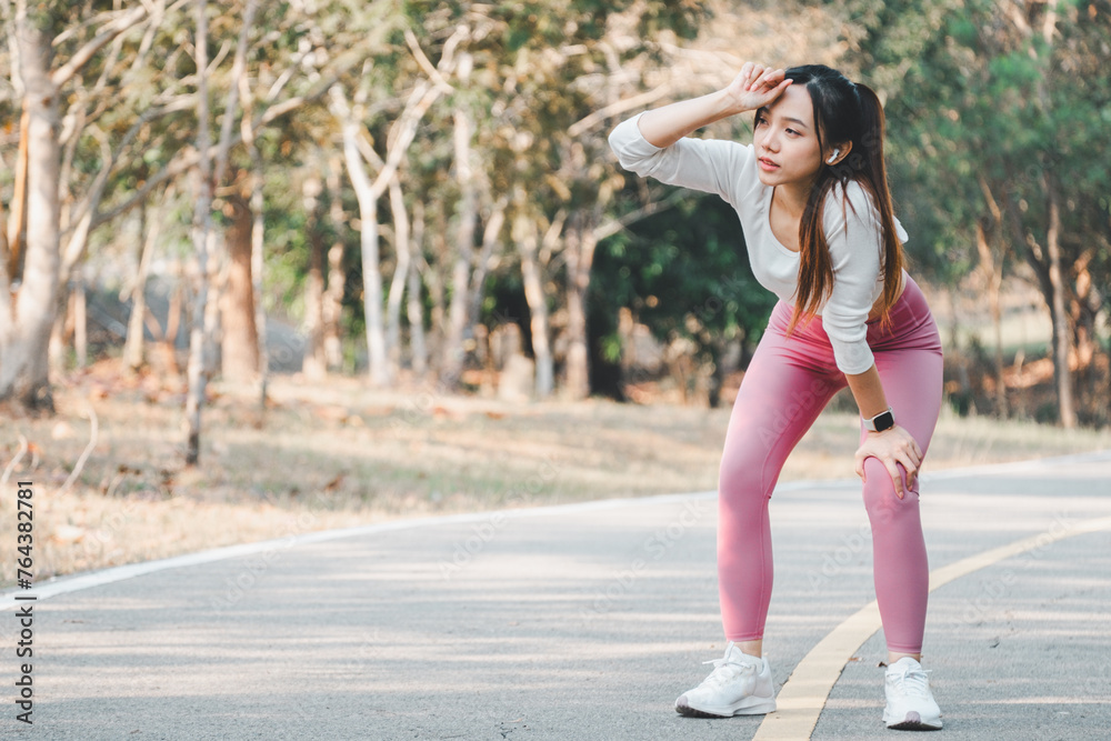 A young athlete takes a moment to cool down, wiping sweat from her brow after a vigorous workout on a park trail, illustrating the importance of rest in fitness regimes.