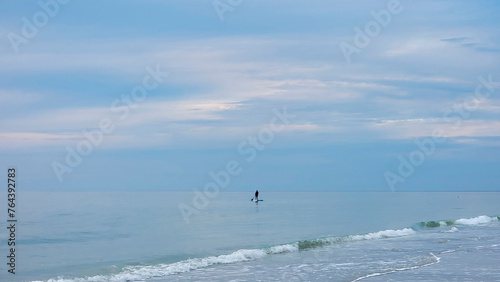 Lone Paddleboarder in the Gulf: Panoramic Redington Beach, Florida. Tranquil Sunset Paddle. Silhouette at Golden Hour. Calm Ocean Water, Sandy Beach Shoreline. Scenic Paddleboarding Photo, Watersports