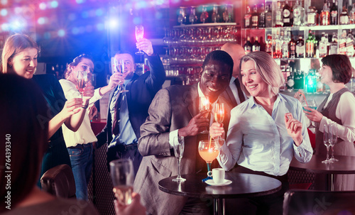Cheerful African businessman having fun with mature female coworker during office party at nightclub