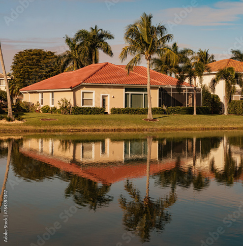Typical concrete house on the shore of a lake in southwest Florida in the countryside with palm trees, tropical plants and flowers, lawn and pine trees. Florida.