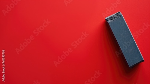A single black eraser on a bright red background with a shadow photo