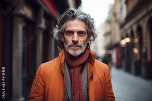 Portrait of a handsome middle-aged man in an orange jacket and red scarf on the street.