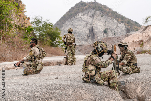 Soldiers in camo gear during a tactical operation with binoculars and rifles on a rocky terrain, showcasing military precision and readiness.