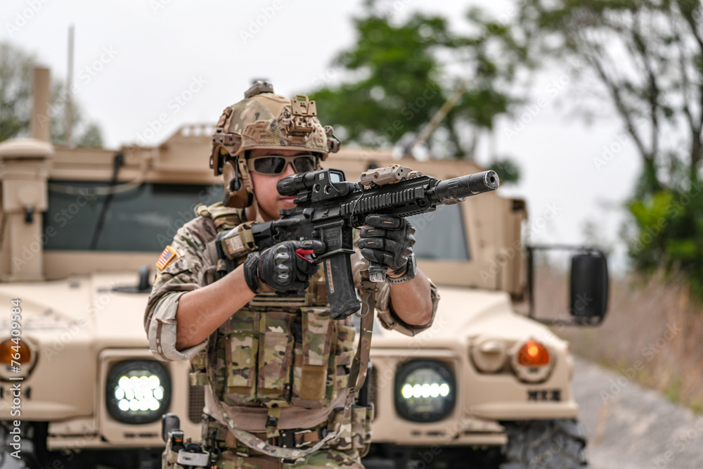 Fototapeta premium Confident soldier in full gear stands before a military vehicle, rifle in hand, showcasing readiness and strength.
