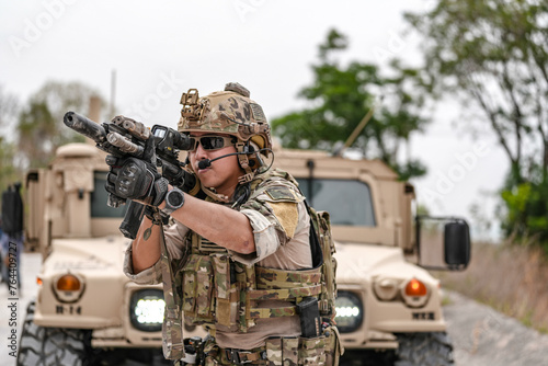 Confident soldier in full gear stands before a military vehicle, rifle in hand, showcasing readiness and strength.