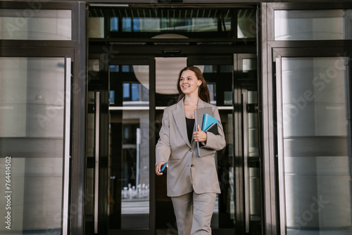 Businesswoman exiting building with notebooks and smartphone.