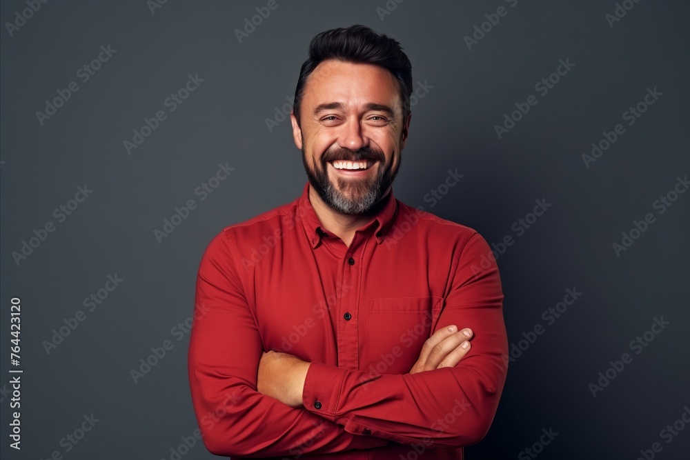 Portrait of a handsome bearded man in a red shirt smiling at the camera while standing against grey background