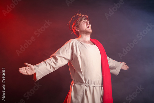 Man in Jesus robe and crown of thorns screaming with smoke on black background