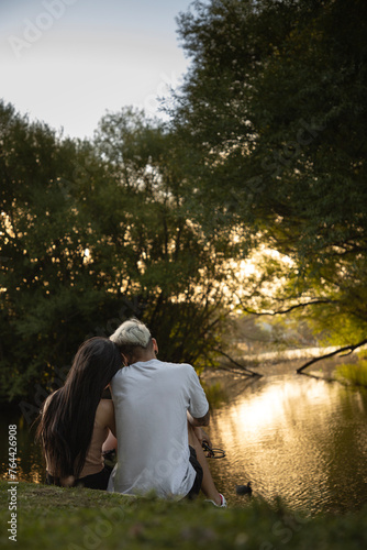 pareja de enamorados sentados a la orilla de un lago de espaldas a camara mirando el aterdecer a contraluz