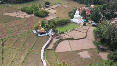 Top view of a bamboo bridge to white pagoda and Phra Chao Ton Luang a large outdoor golden Buddha statue. Sitting in the middle of a rice field at Wat Nakhuha there are beautiful natural places. 