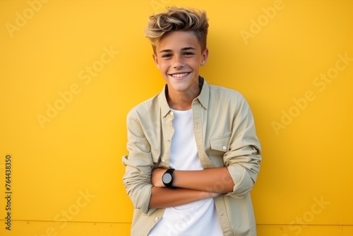 Portrait of a handsome teenage boy smiling against a yellow wall.
