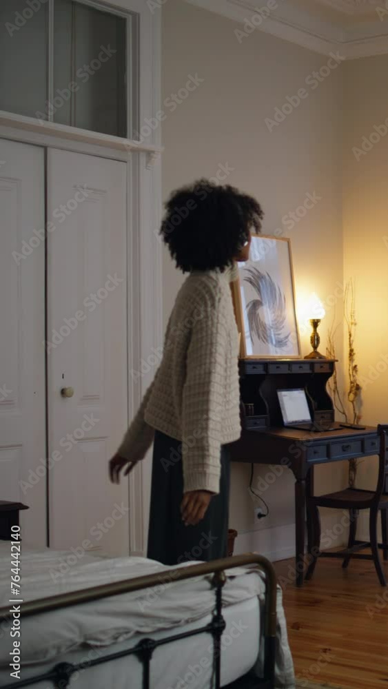 Positive lady crossing bedroom at evening. Curly woman enjoying music vertically Positive lady crossing bedroom at evening. Curly woman enjoying music vertically