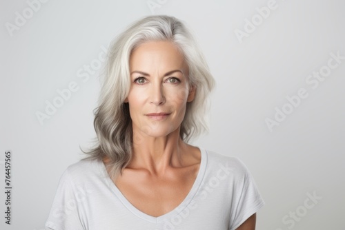 Mature woman with grey hair looking at camera, over grey background © Inigo
