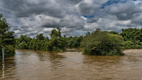 A turbulent river flows in a tropical rain forest. The riverbed divides into channels, skirting islands with lush green vegetation. Clouds in the blue sky. Iguazu river. Argentina