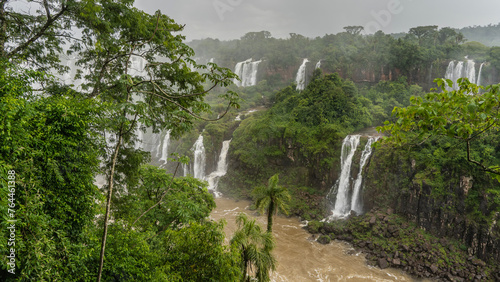 Tropical waterfall landscape. Streams of water cascades from a cliff into a stormy river. Splashes, fog all around. Lush green vegetation. Iguazu Falls. Brazil