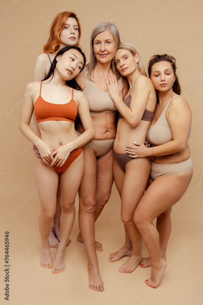 Cheerful, attractive, diverse women wearing stylish underwear, hugging and looking at camera
