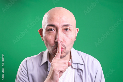 Asian bald man keeps finger on lips, asks not tell secret information or keep silence © Gatot