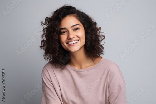 Portrait of a smiling young woman with curly hair against grey background