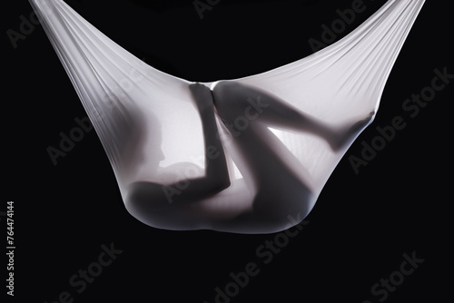 Person, fabric and wrapped naked in studio, abstract and creative art on black background. Woman, girl and material for ethereal or phantom ghost, bare and nude in sheet for fetus illusion in cloth